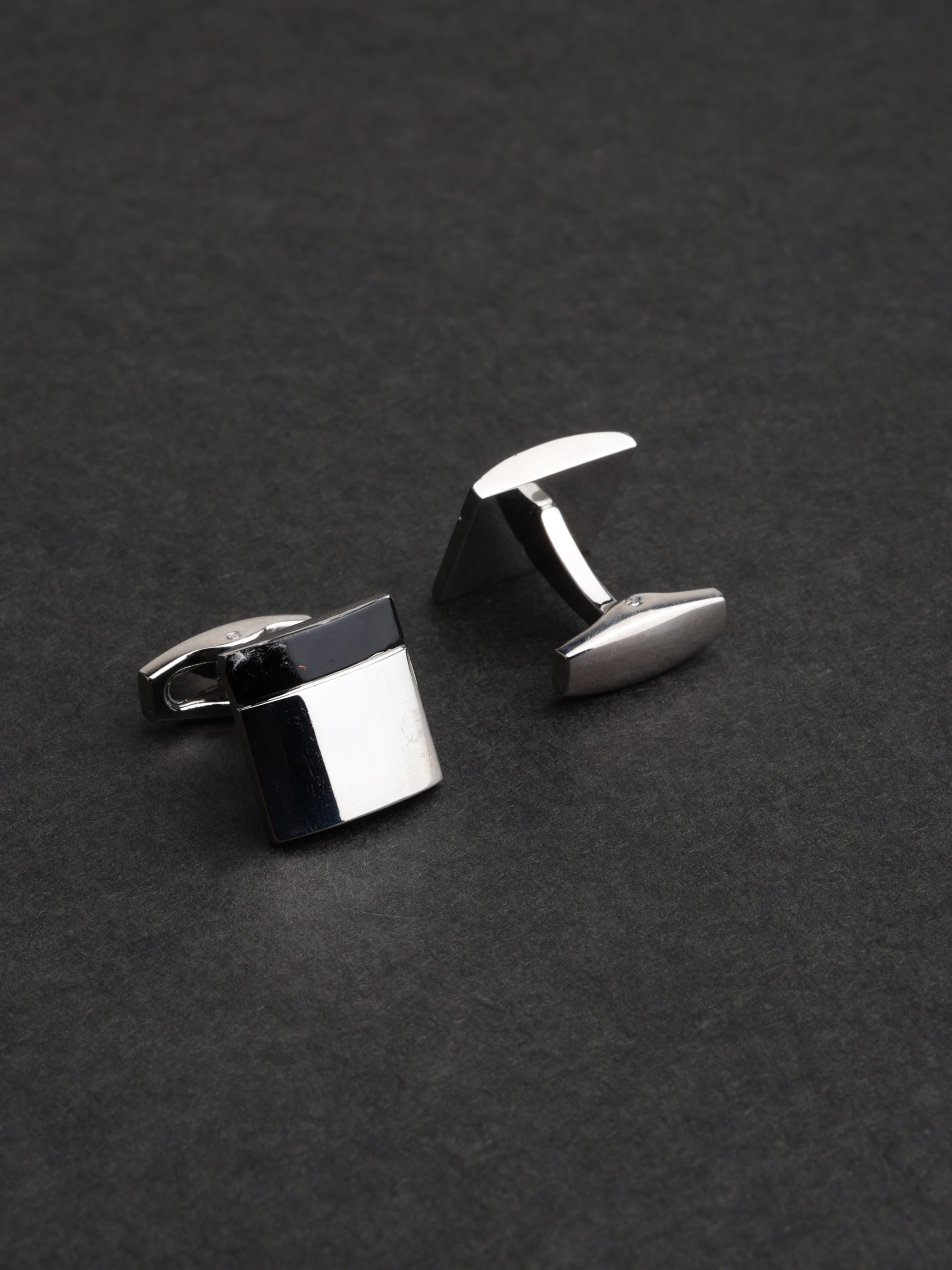 Silver cufflinks on a dark gray background