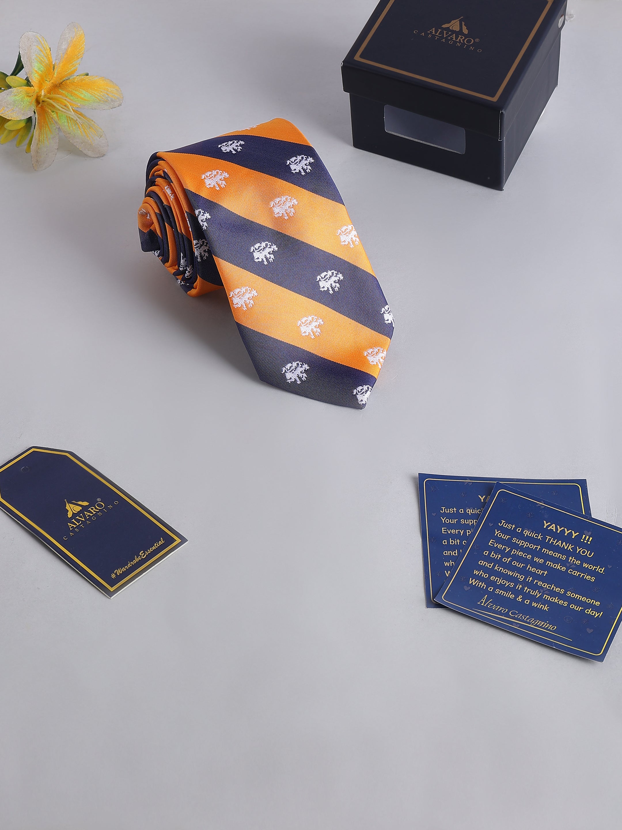 Orange and navy striped tie with floral pattern, accompanied by a box and cards on a light gray surface.
