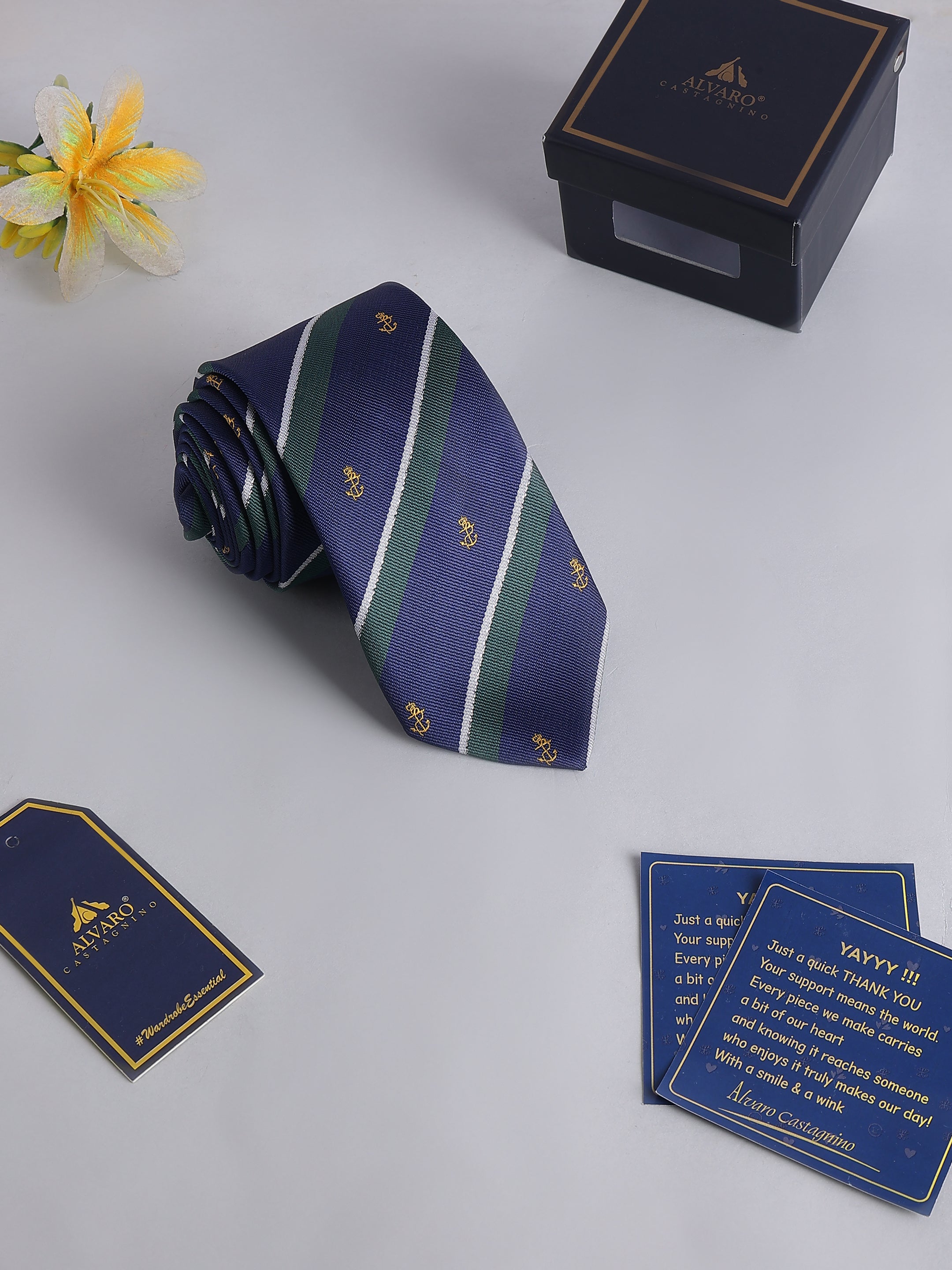Navy striped tie with gold accents on a light gray surface, accompanied by a box and cards.