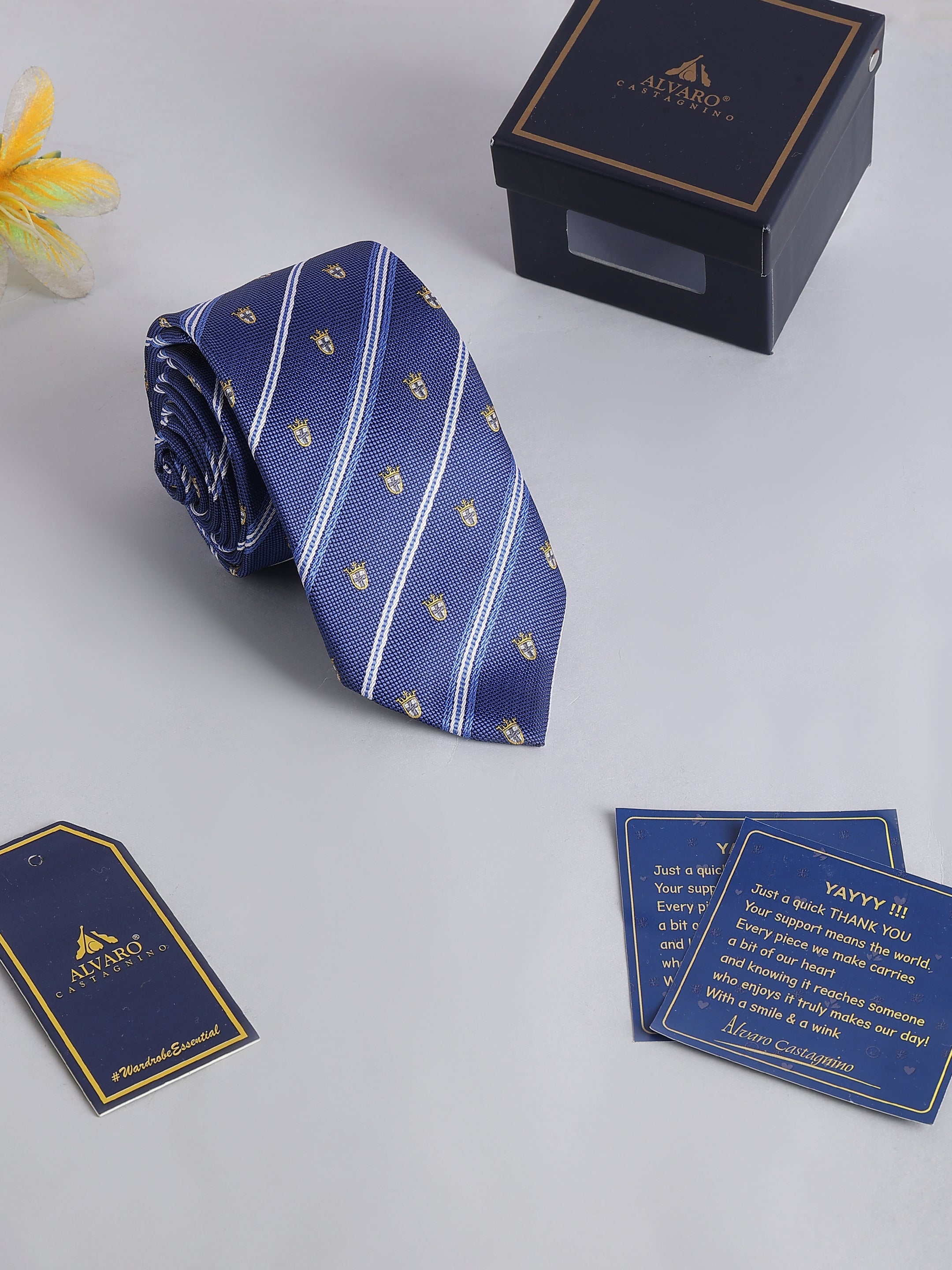 Blue striped tie with gold patterns, packaging box, and cards on a light gray background