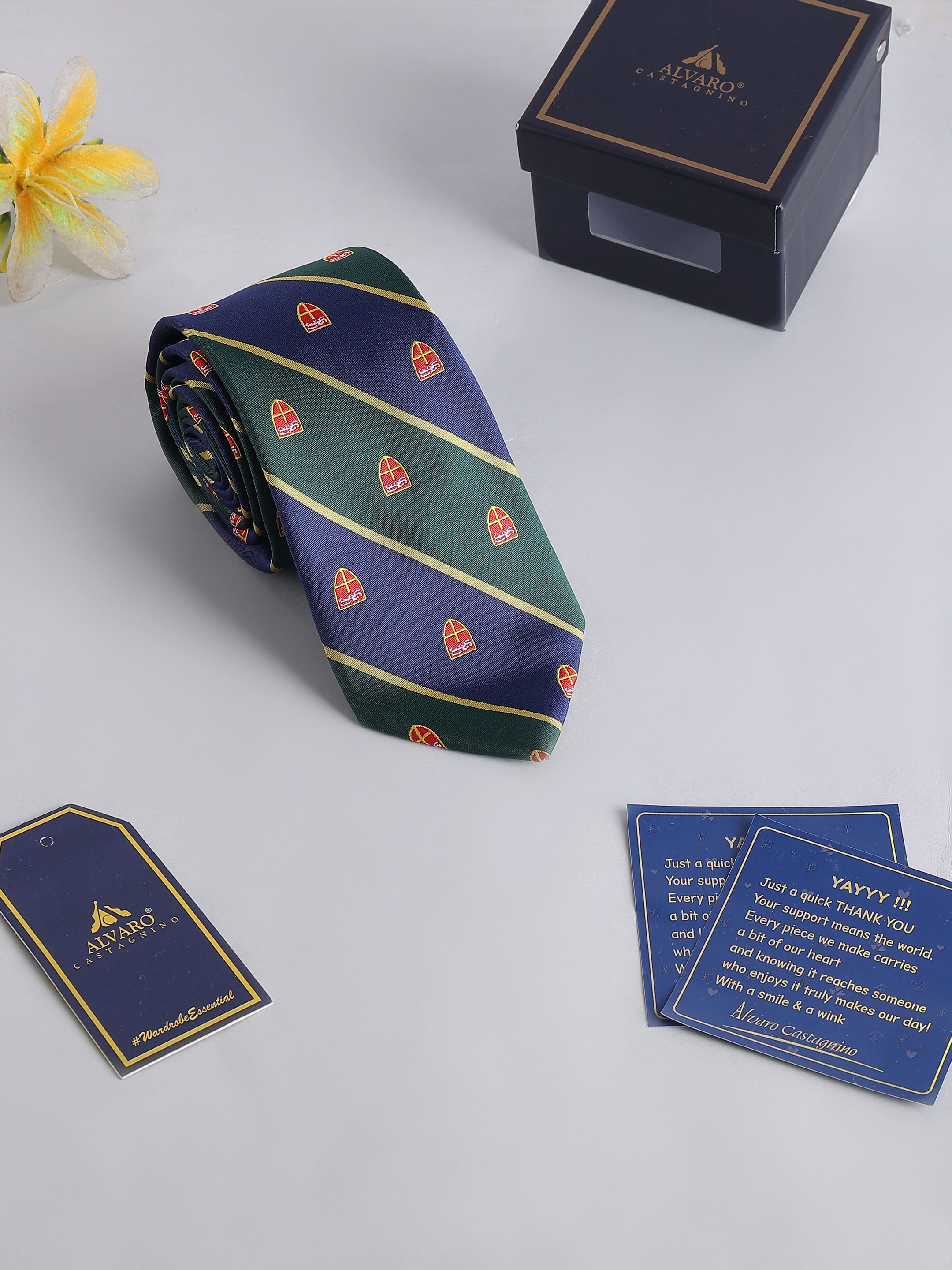 Navy and green striped tie with red patterns, placed on a light gray surface with a branded box and cards.