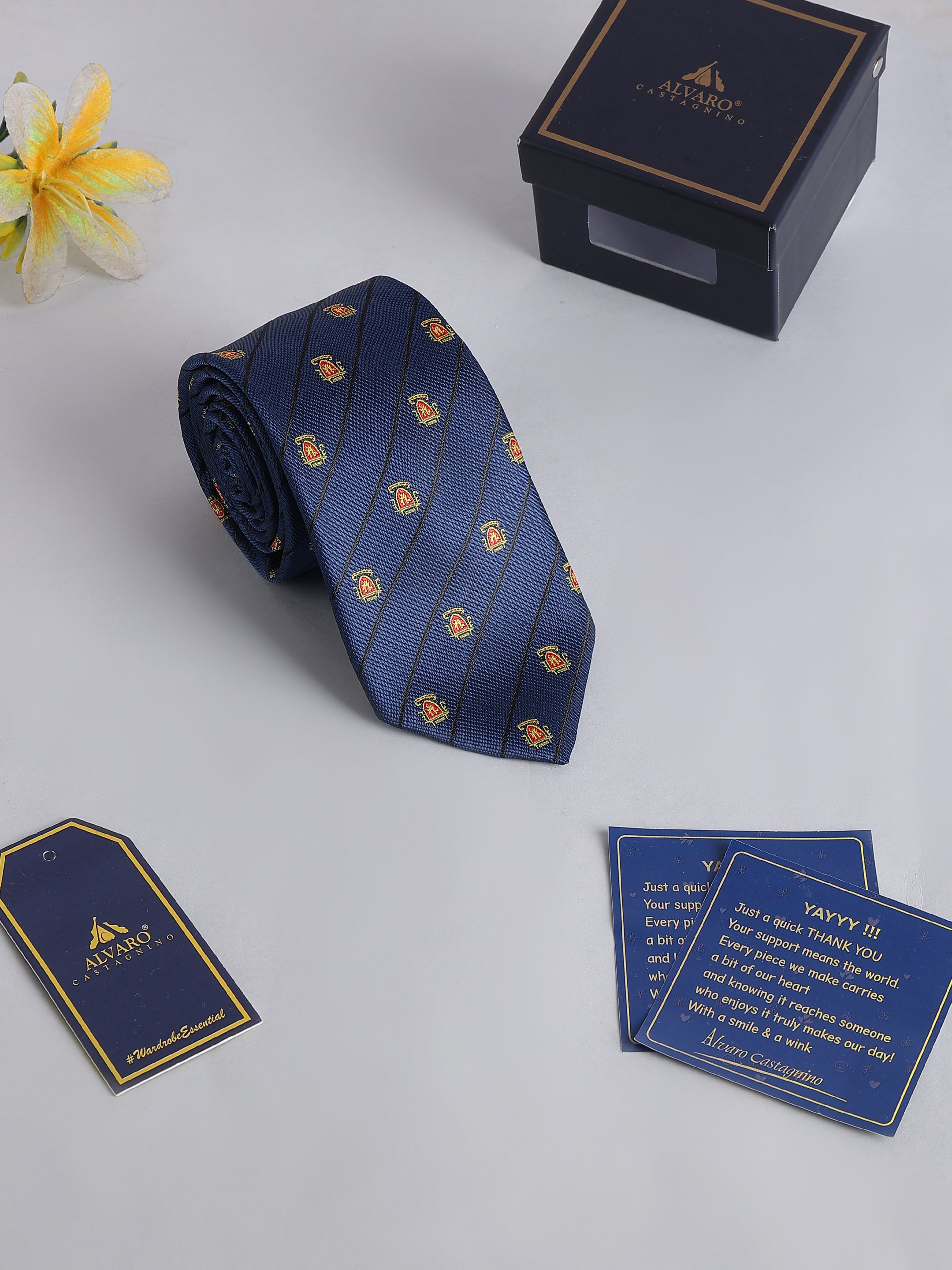 Navy blue tie with gold patterns, accompanied by a box and cards on a light gray background.