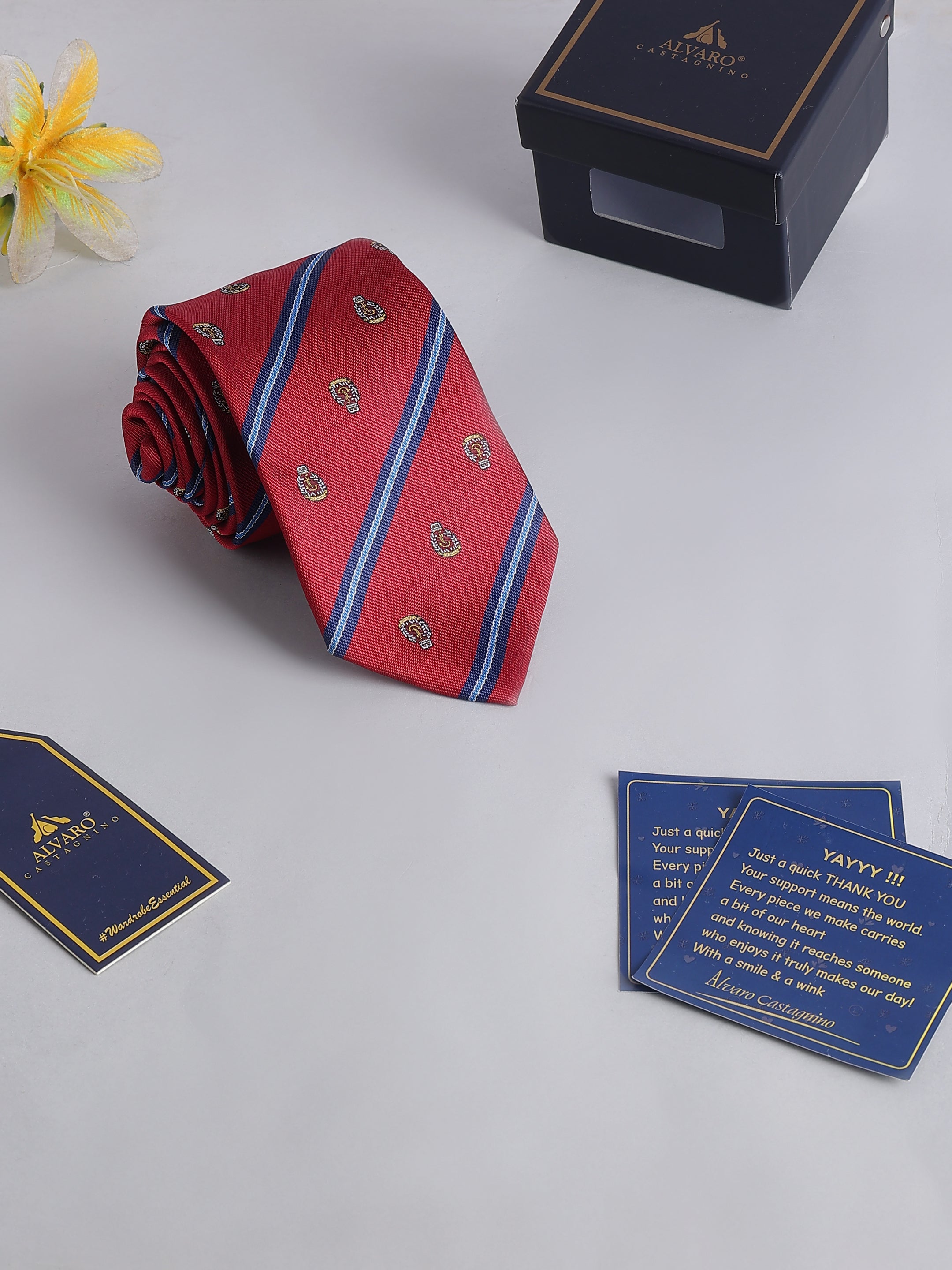 Red striped tie with blue accents on a light gray surface, accompanied by a box and cards.
