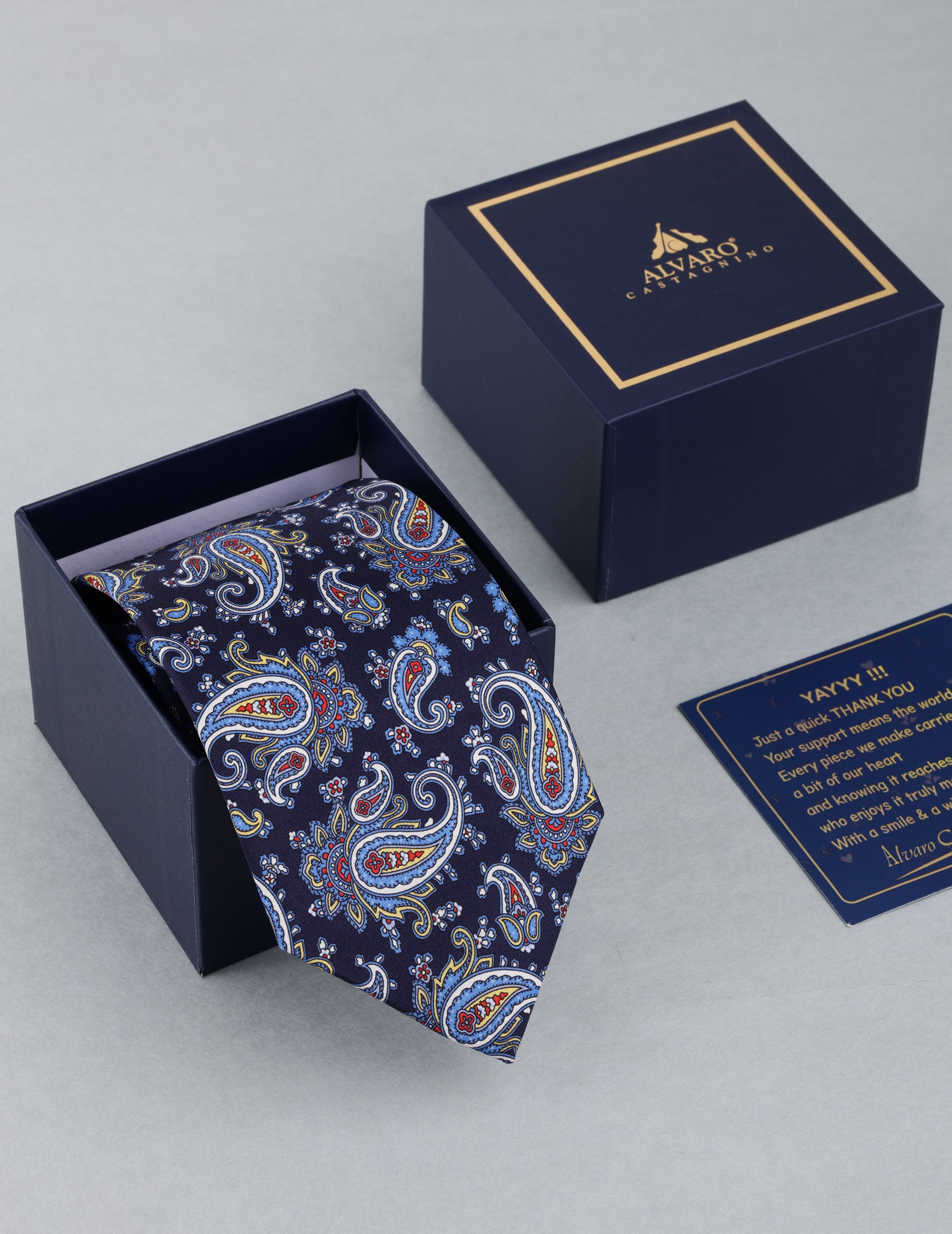 Navy paisley tie in a branded box with a card on a light gray background