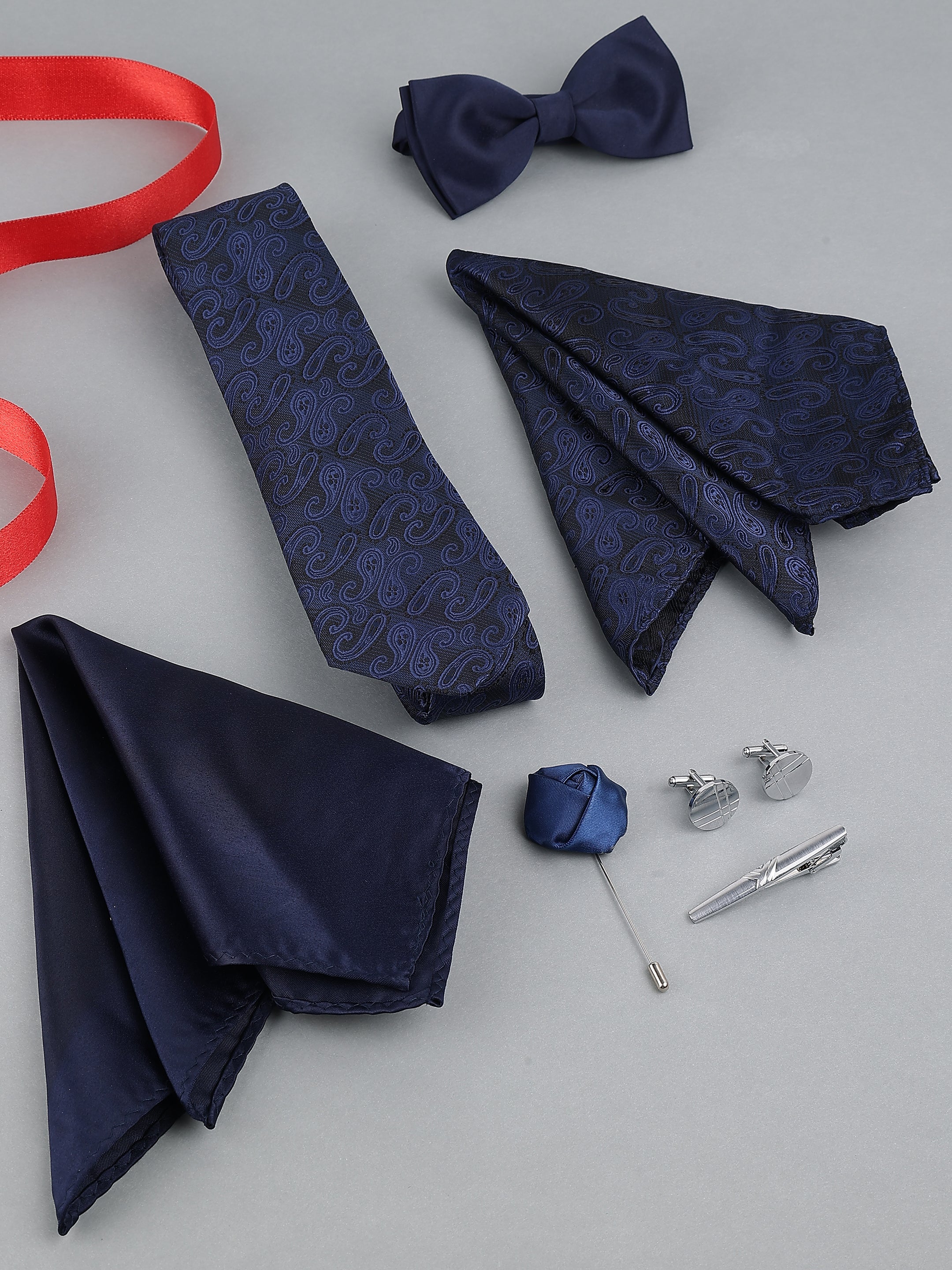Navy blue tie, pocket square, bow tie, cufflinks, and accessories on a light gray background