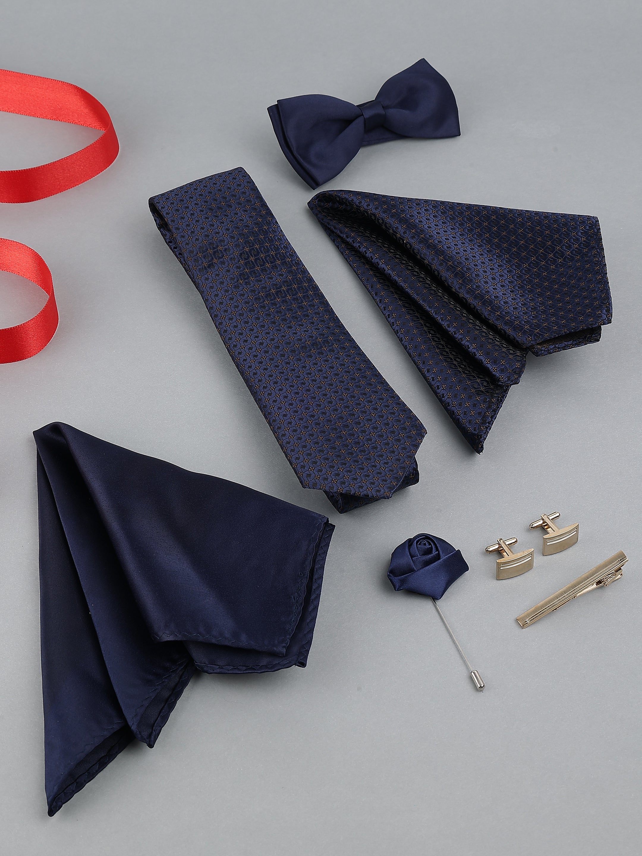 Navy blue tie, pocket square, bow tie, cufflinks, and lapel pin on a gray background